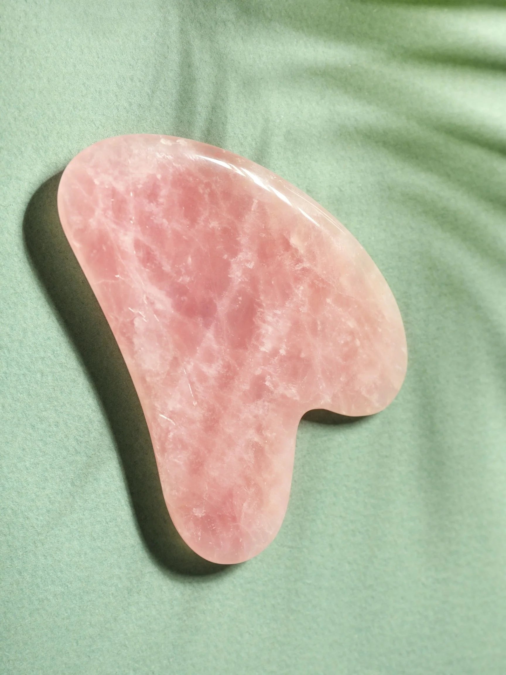 Pink gua sha tool on a green fabric background