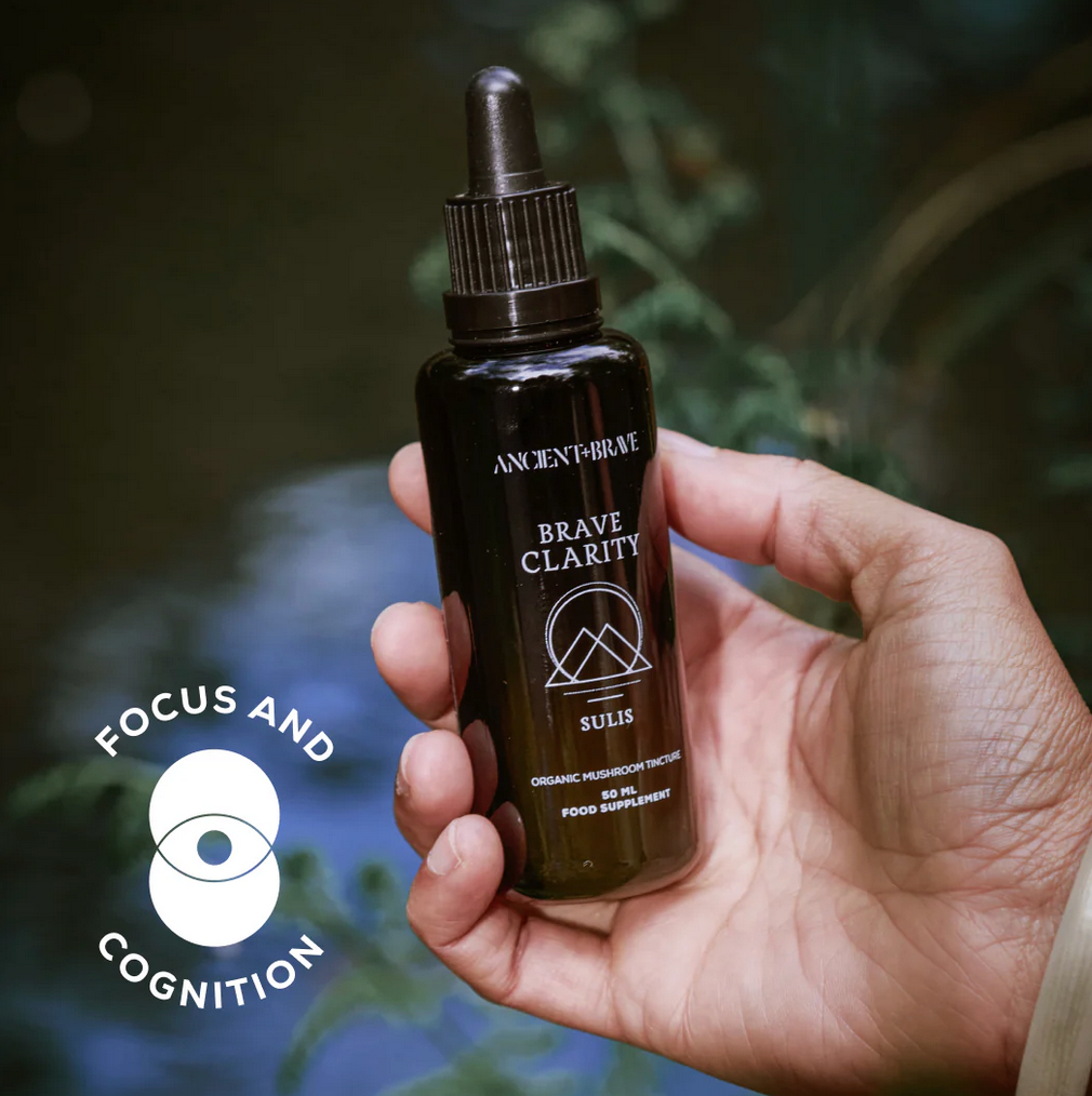 Hand holding a bottle labeled &#39;Brave Clarity&#39; with a blurred natural background