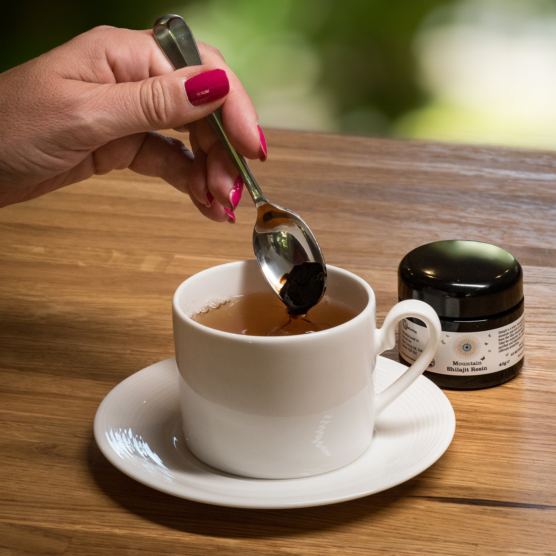 Person adding honey to a cup of tea on a wooden table