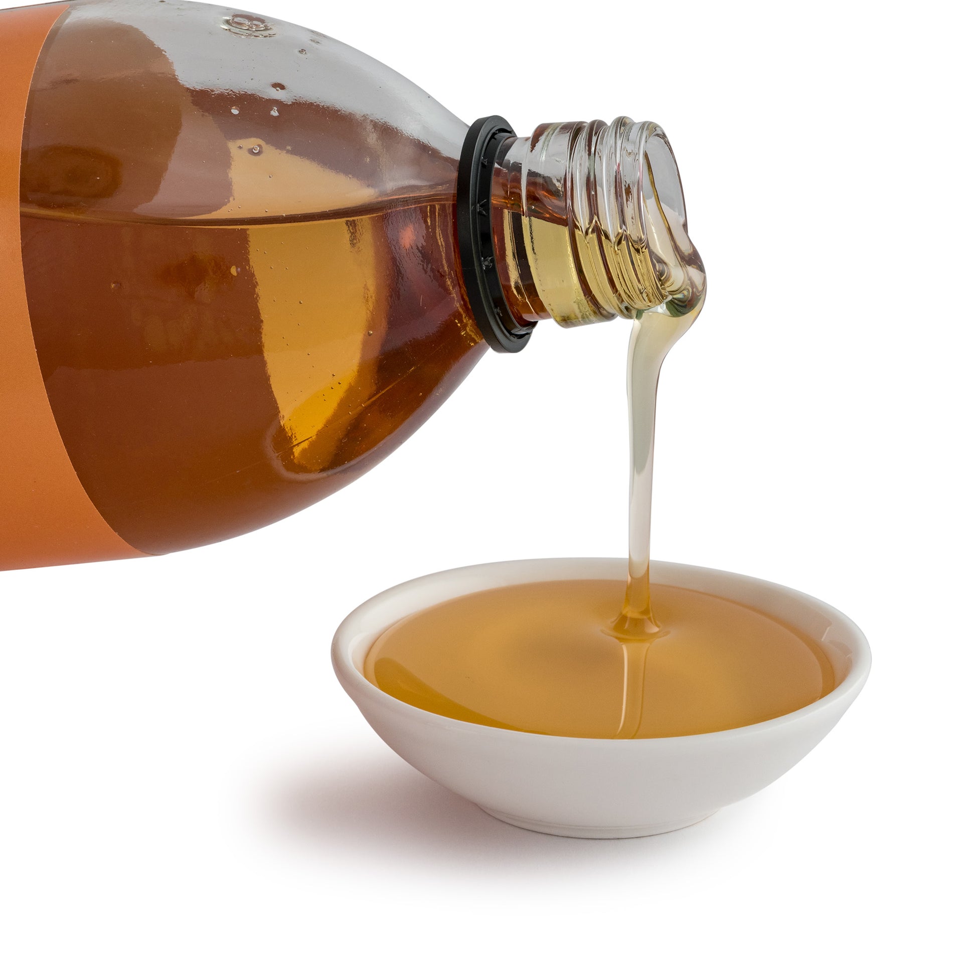 Amber-colored bottle pouring liquid into a white bowl on a white background