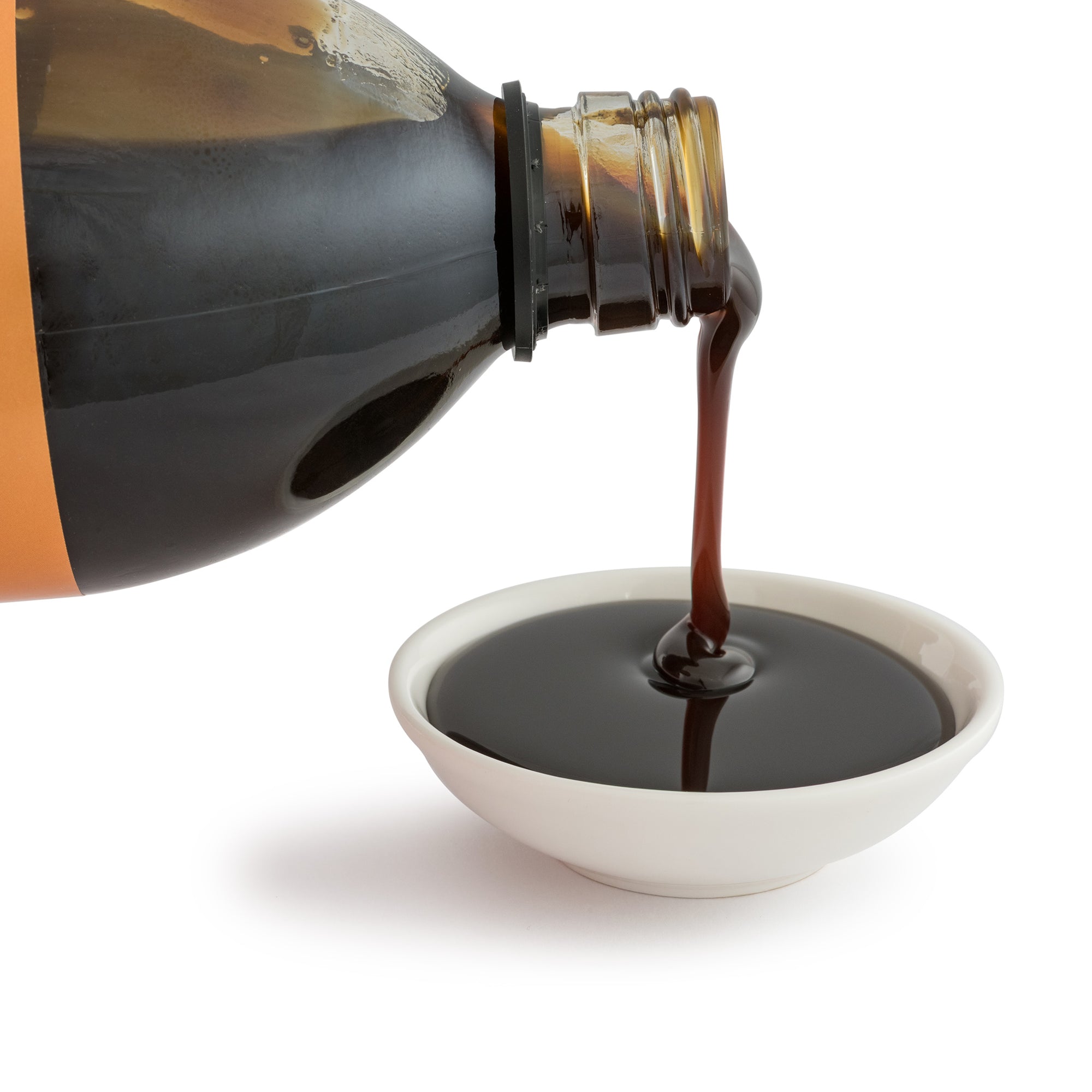 Bottle pouring dark liquid into a white bowl on a white background