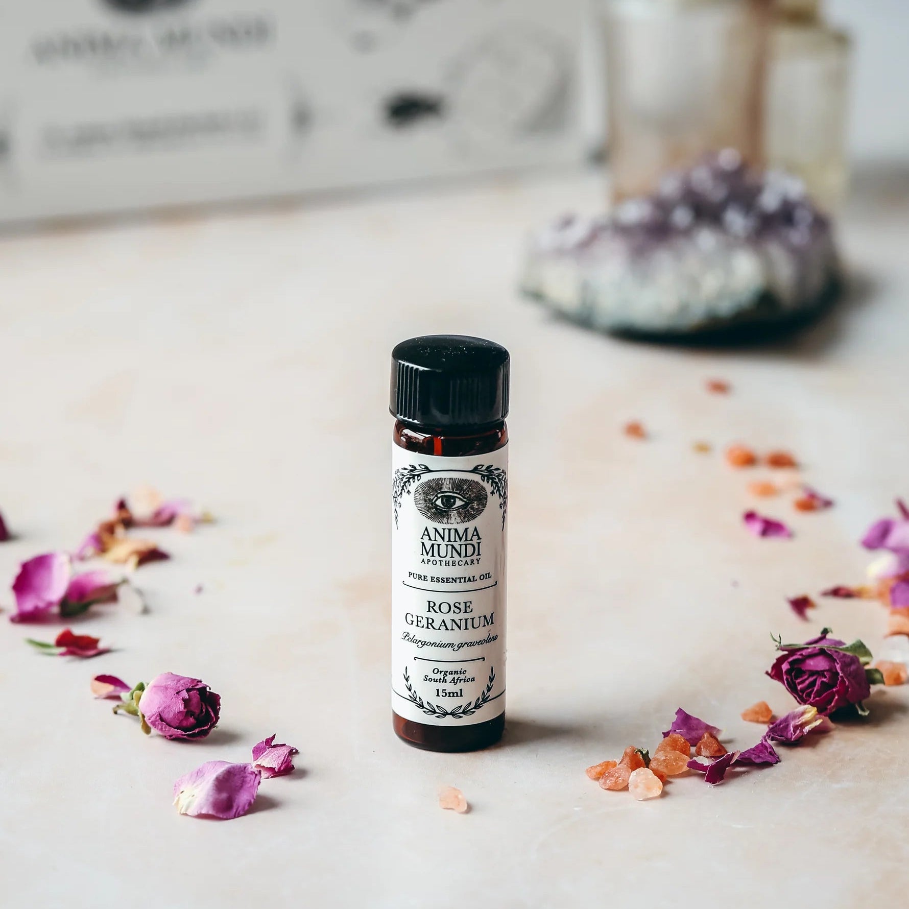 Small bottle of rose geranium essential oil with flowers on a light surface