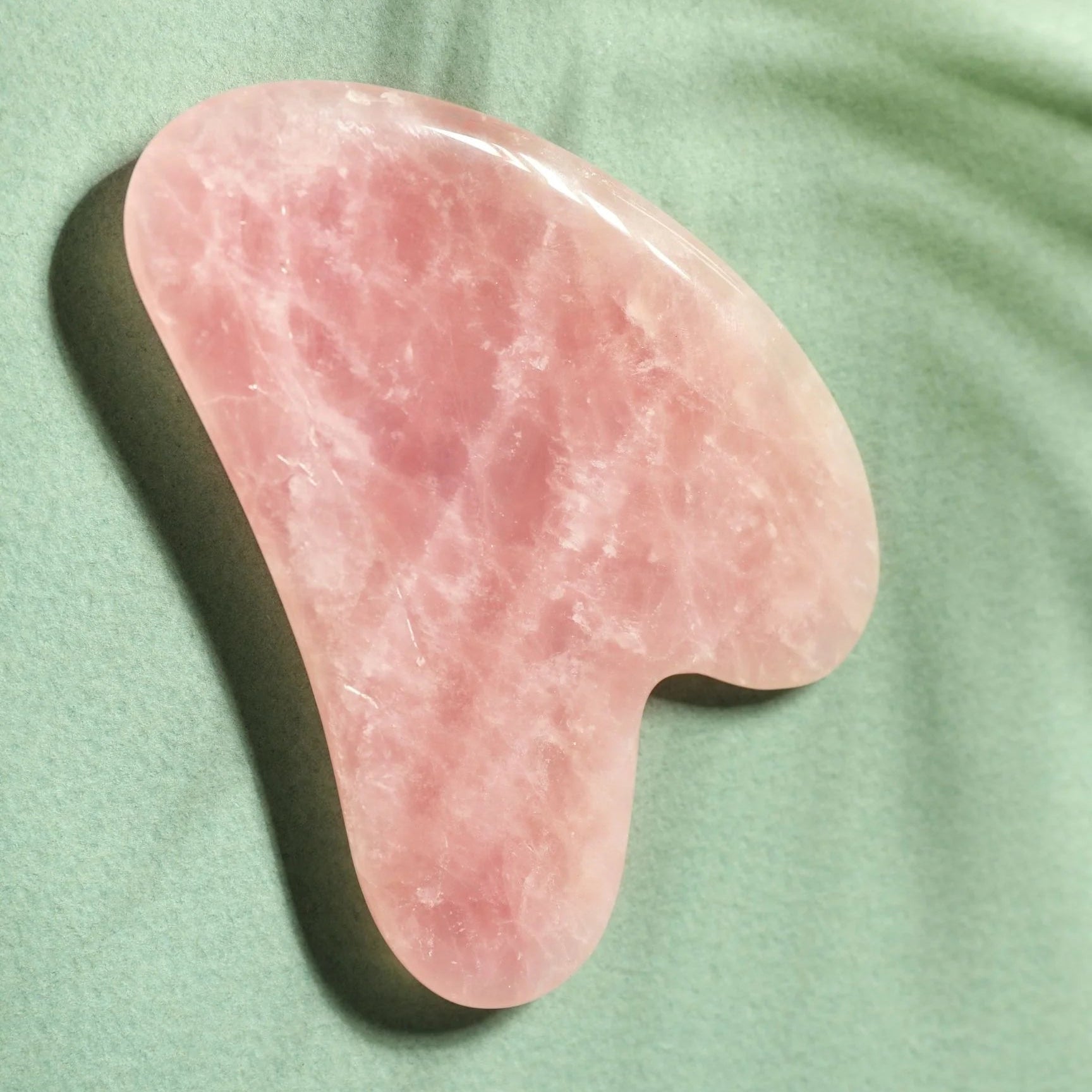 Pink gua sha tool on a green fabric background
