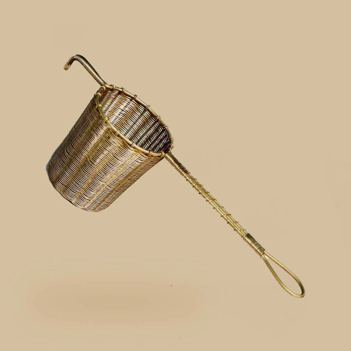 Brass strainer with handle on a beige background