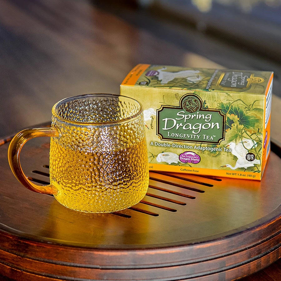 A glass cup of Spring Dragon Longevity Tea beside the box on a wooden tray