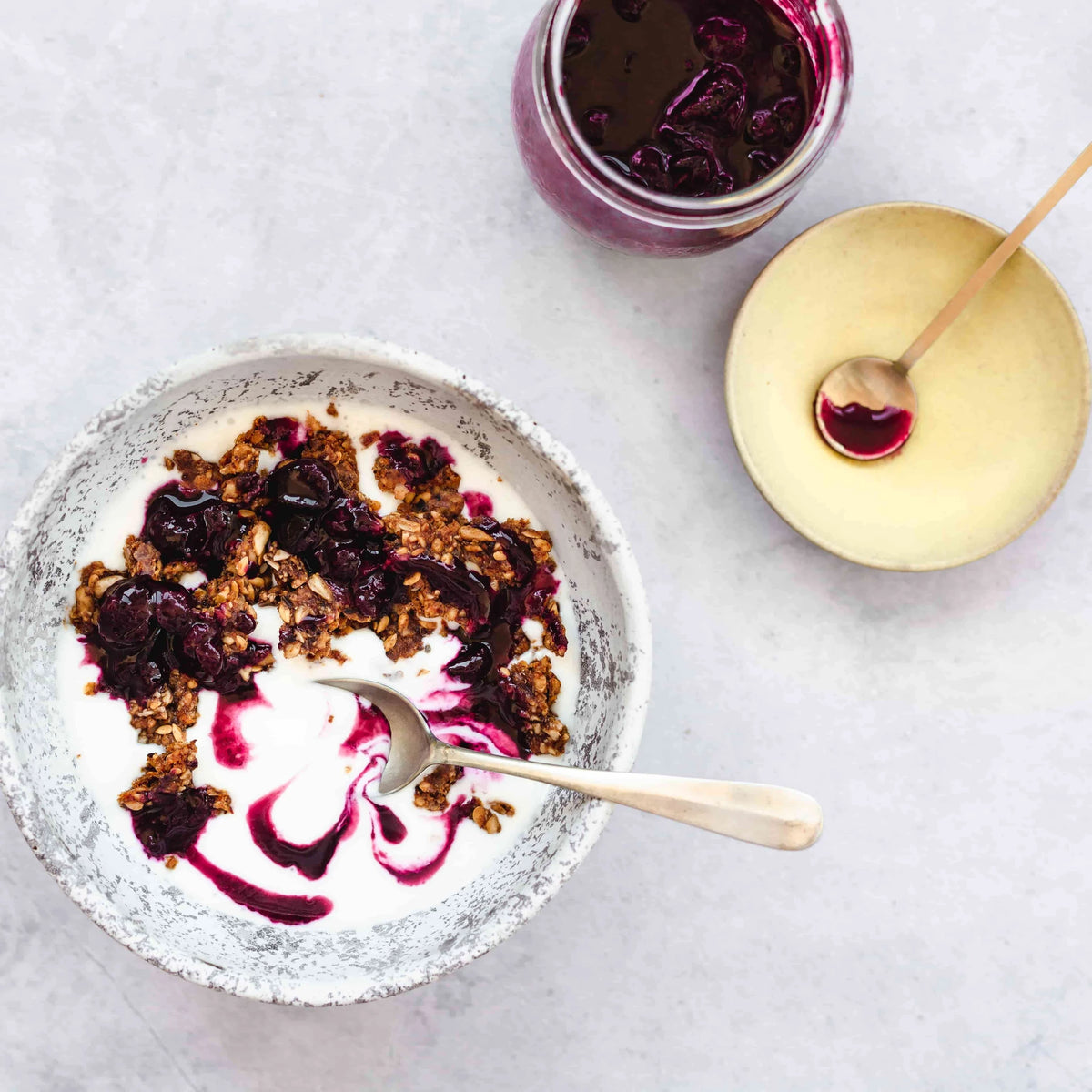 Serving suggestion for Erbology Apple, Chia & Nopal Granola: granola on yoghurt with berry compote in a speckled bowl