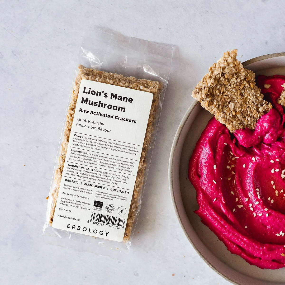 Pack of Erbology Lion's Mane Raw Activated Crackers on a grey stone surface beside a bowl of pink dip with crackers
