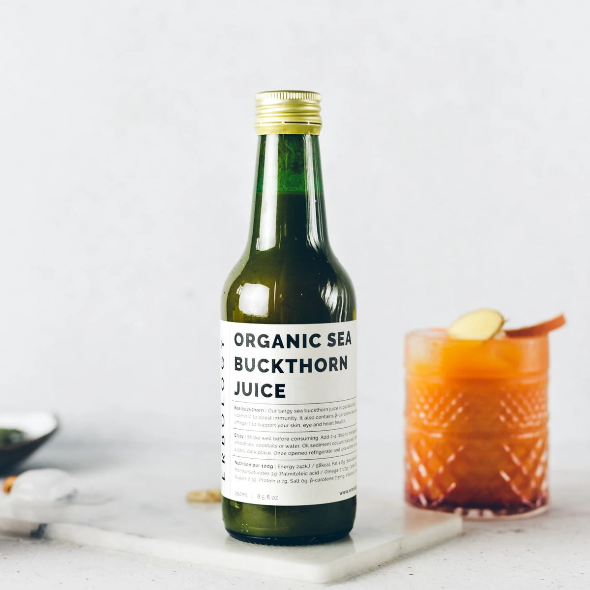 Bottle of Erbology Organic Sea Buckthorn Juice beside a glass of orange drink with a lemon slice