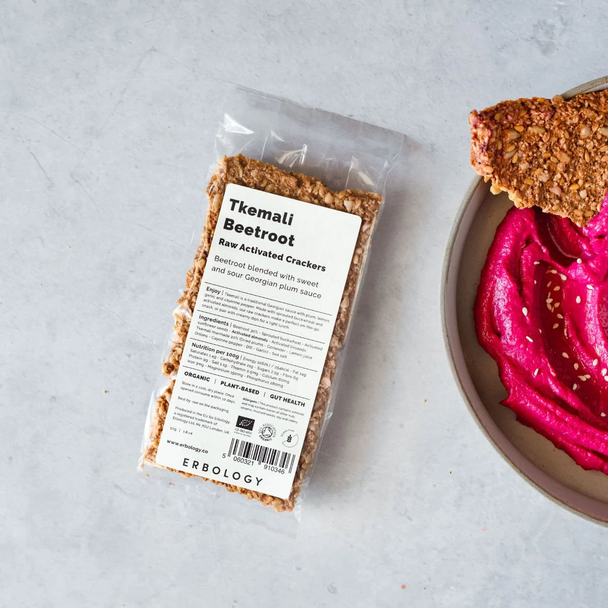 Pack of Erbology Tkemali Beetroot Raw Activated Crackers on a grey stone surface beside a bowl of pink dip with a cracker