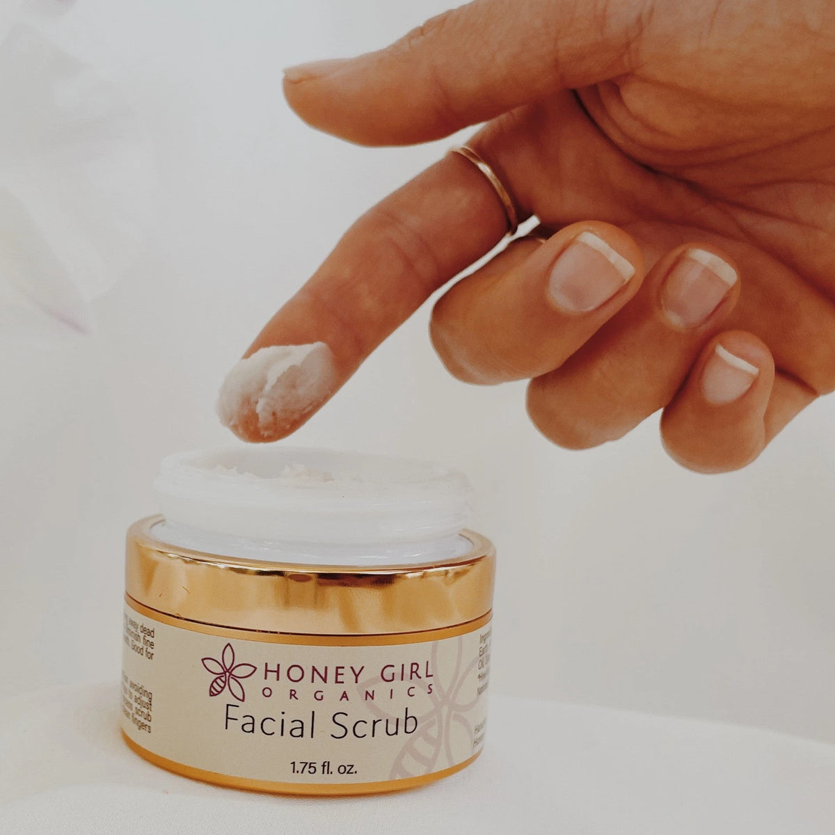 Finger dipping into an open jar of Honey Girl Organics Facial Scrub