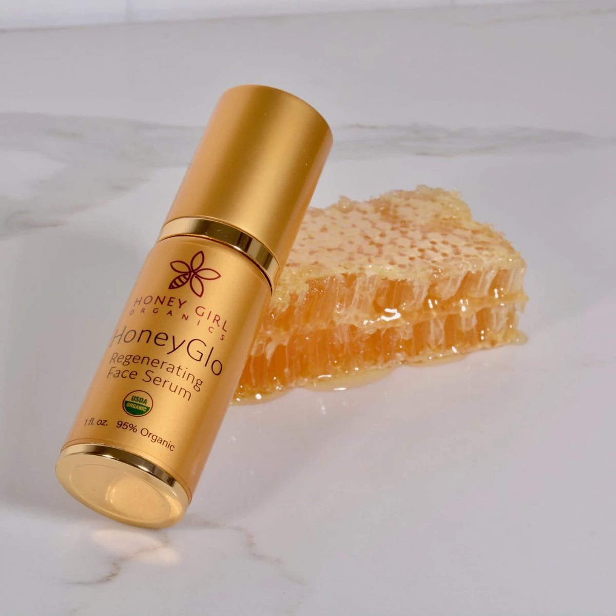 Honey Girl Organics HoneyGlo Regenerating Face Serum bottle beside honeycomb