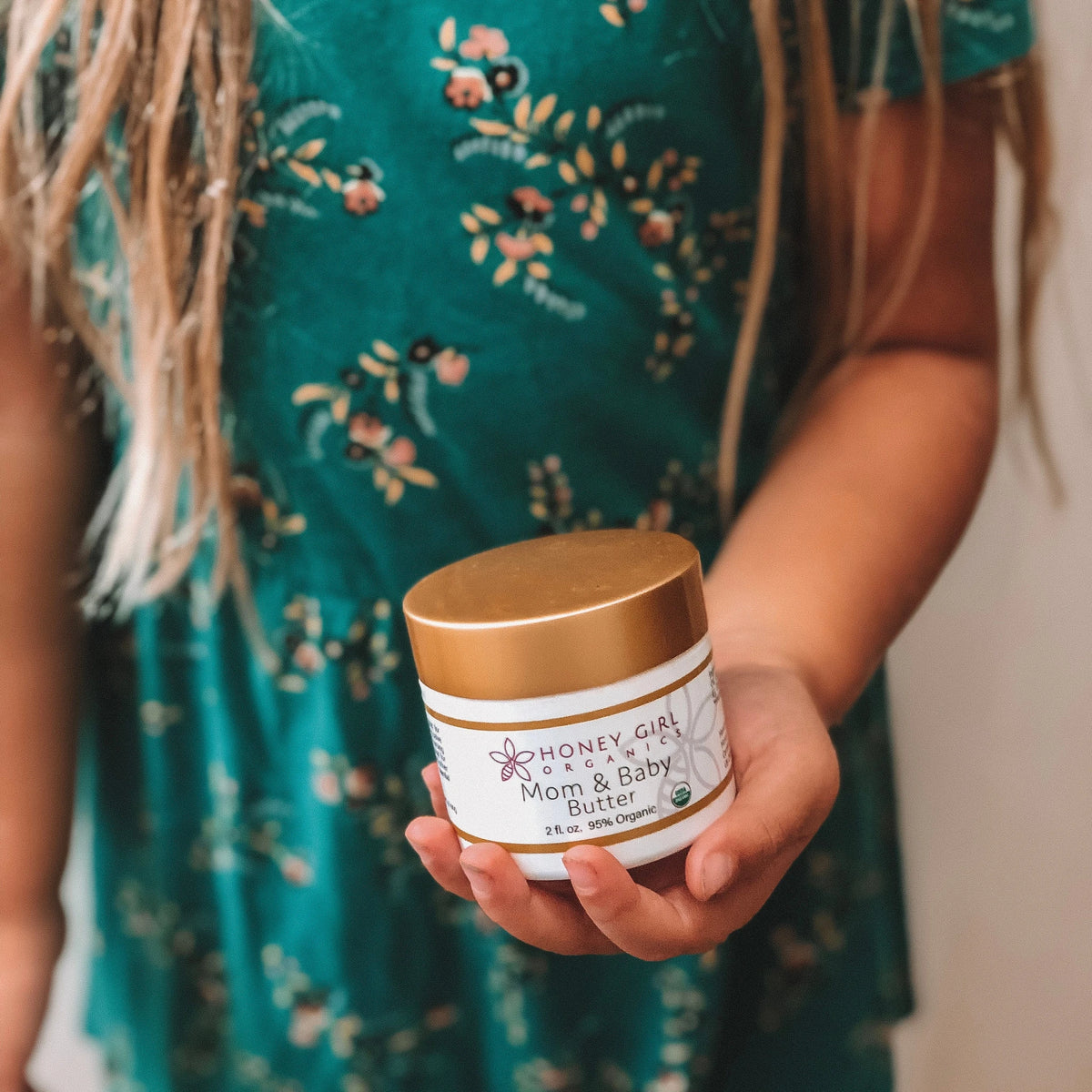 Child in a green floral dress holding a jar of Honey Girl Organics Mom & Baby Butter