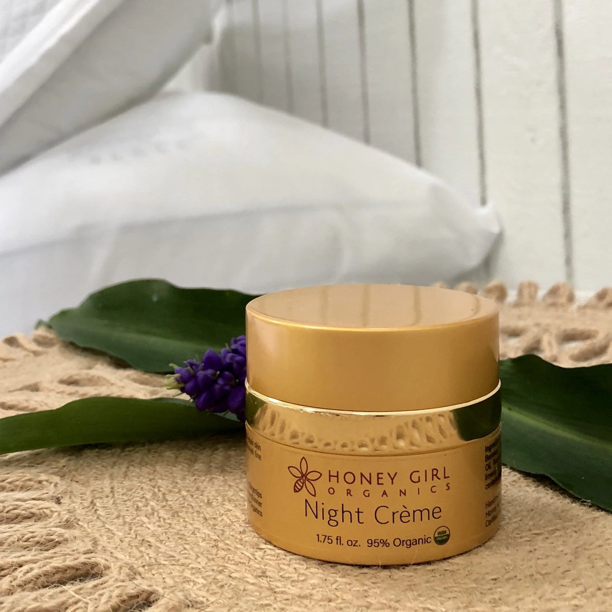 Honey Girl Organics Night Crème jar on a woven mat with tropical leaves