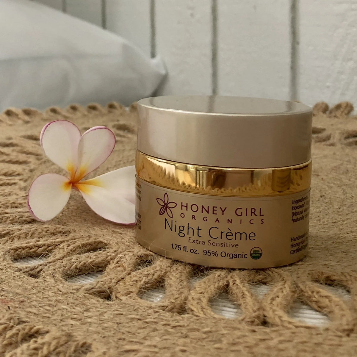 Jar of Honey Girl Organics Night Crème Extra Sensitive on a woven mat with a frangipani flower