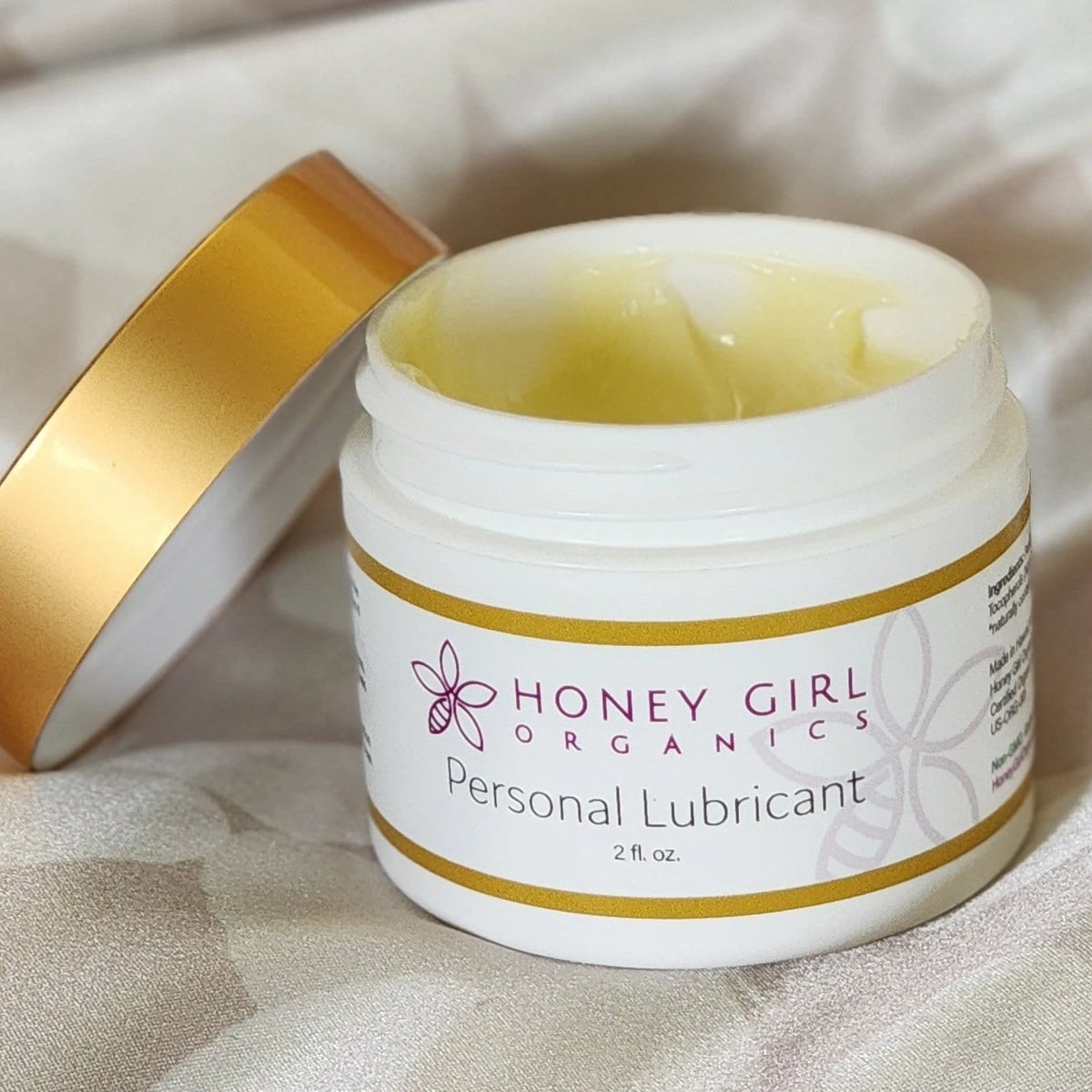 Open jar of Honey Girl Organics Personal Lubricant on white silk