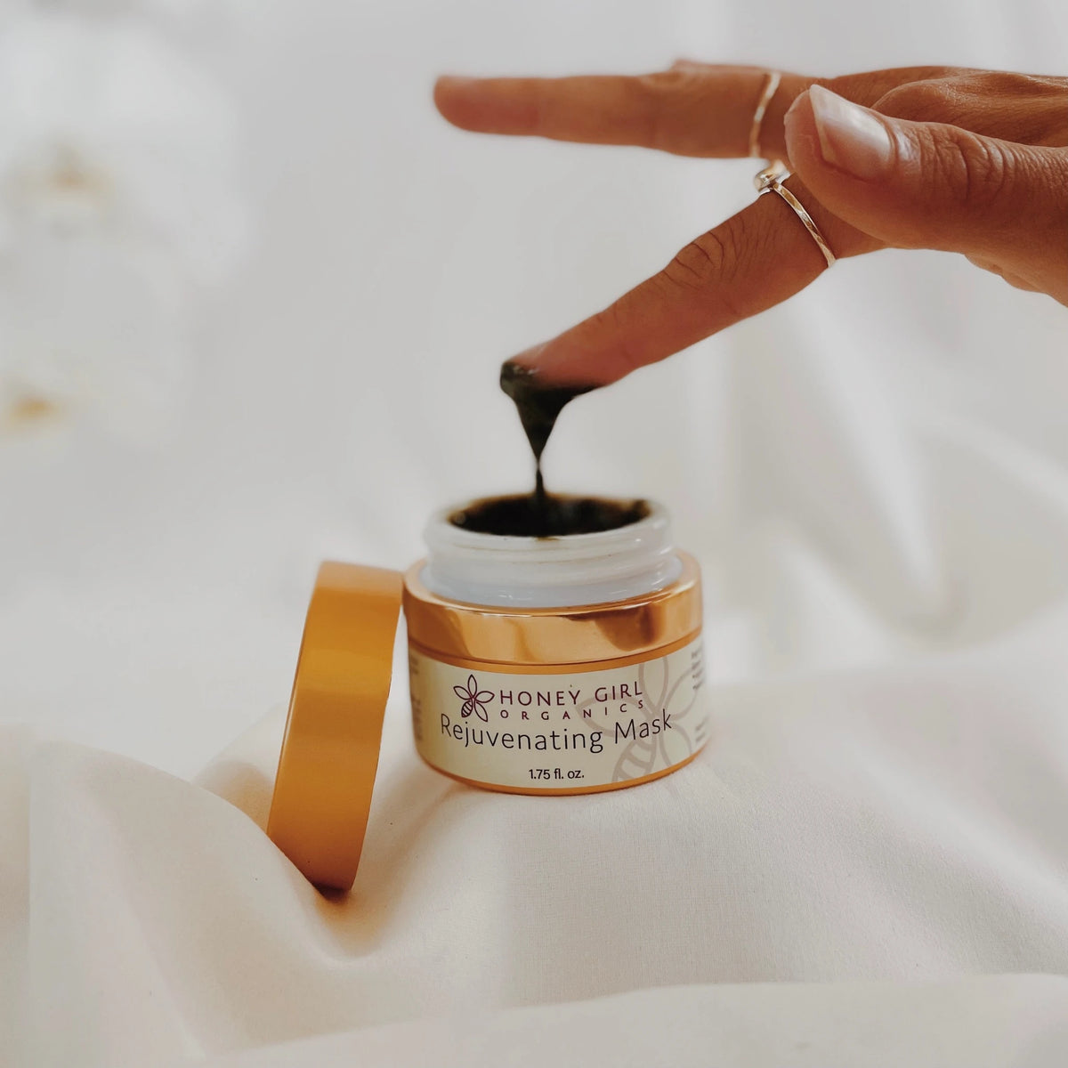Finger lifting dark mask from an open jar of Honey Girl Organics Rejuvenating Mask
