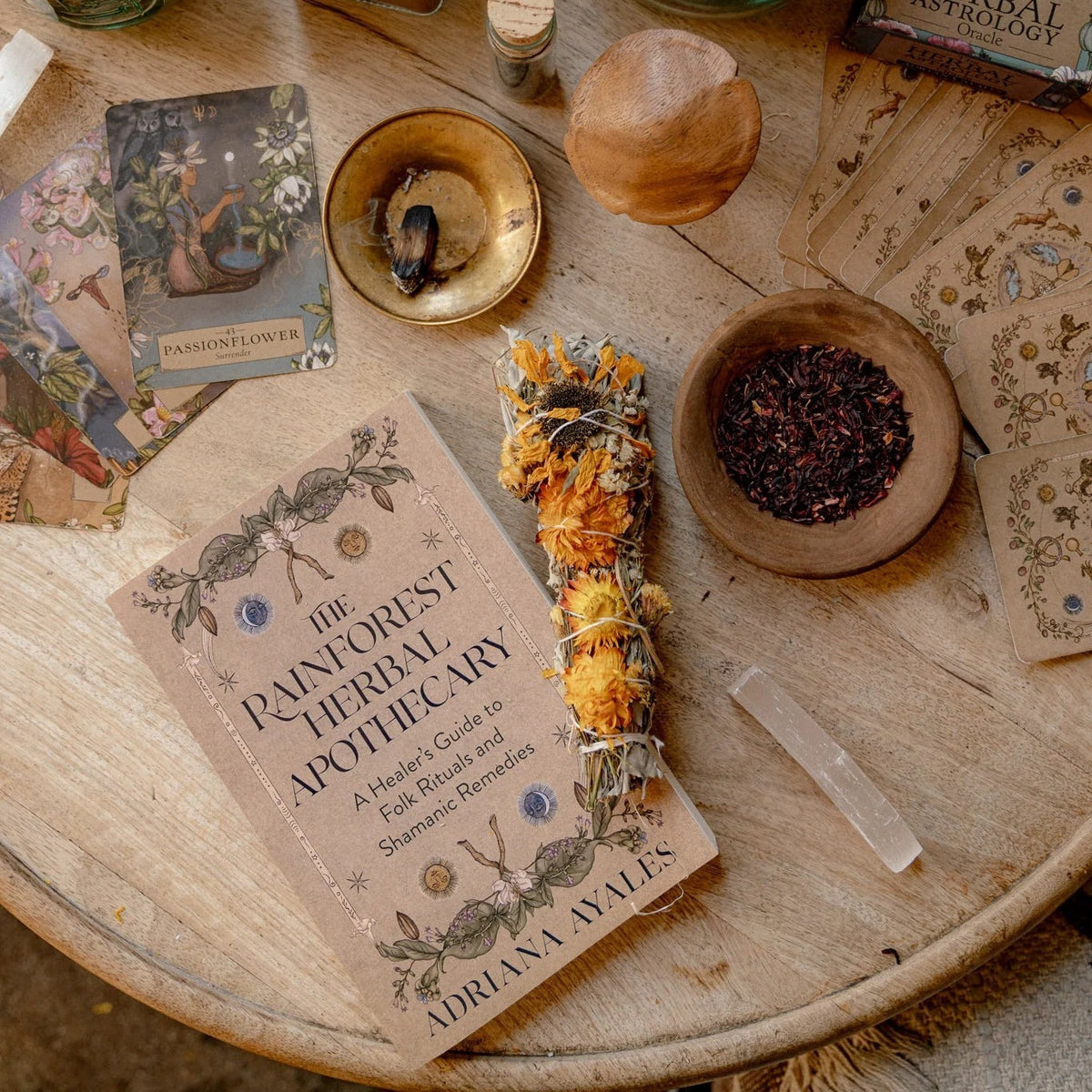 The Rainforest Herbal Apothecary book with dried herbs, a flower bundle and oracle cards