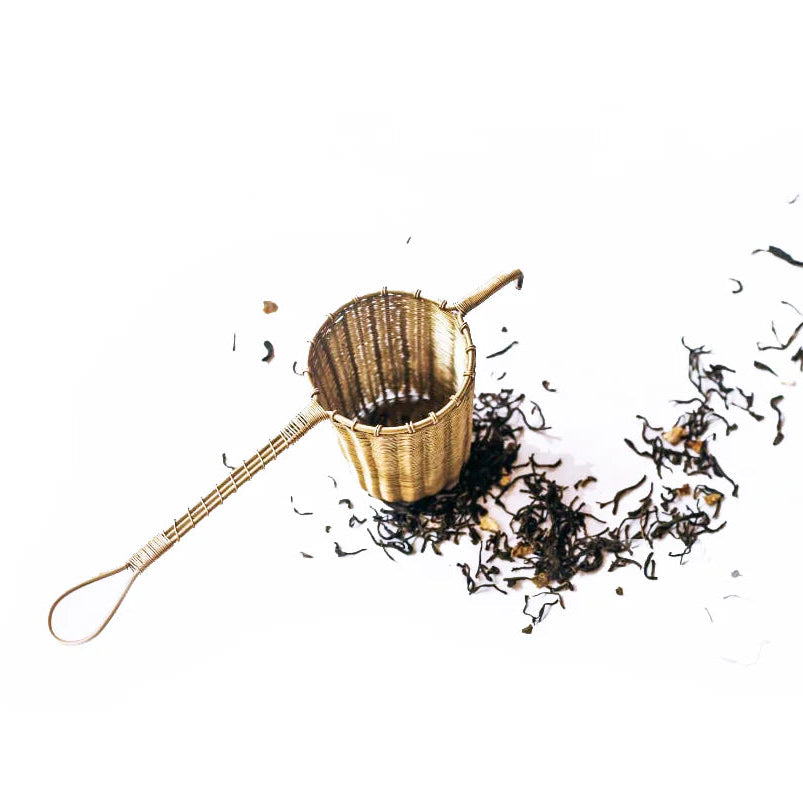 Brass tea strainer with loose tea leaves on a white background